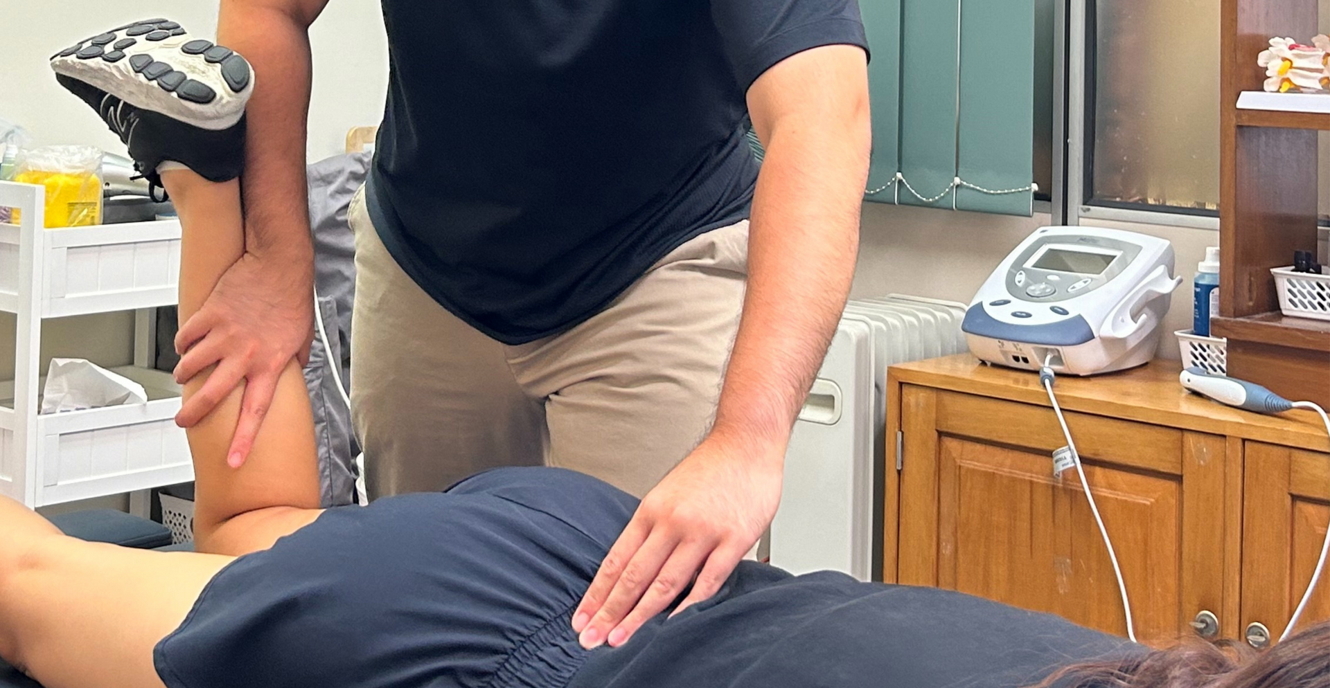 A physical therapist performs a hip stretch on a patient lying on a treatment table in a clinic.