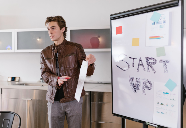 A man is giving a presentation in front of a white board that says start up.
