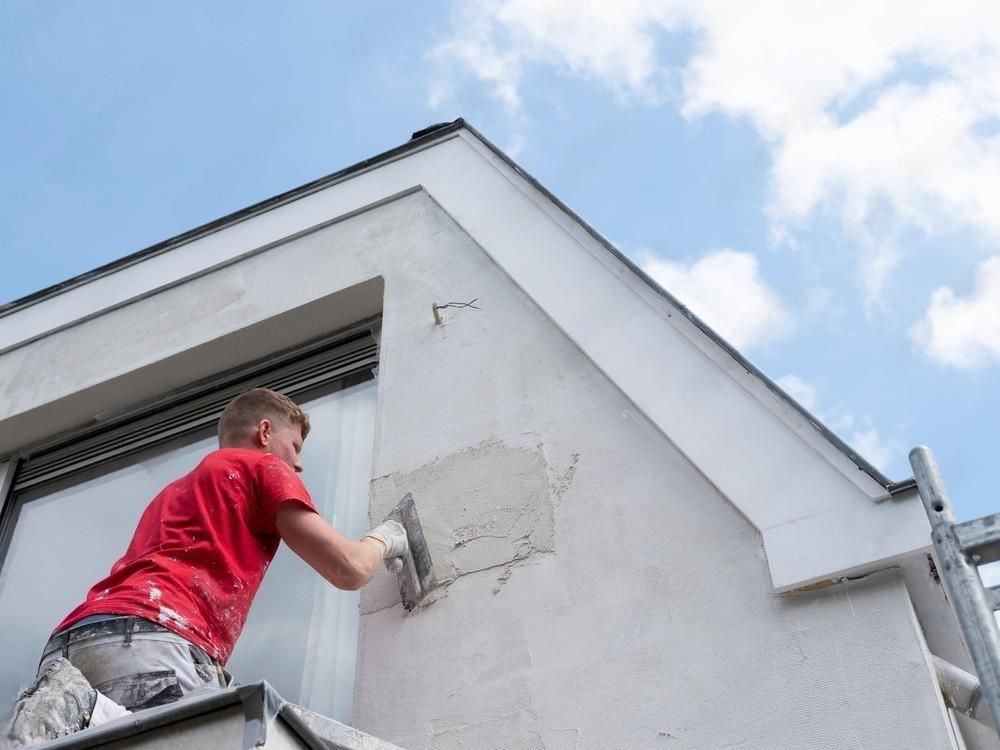 a man is working on the side of a building with a trowel .