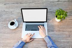 Laptop open on a wooden desk, hands typing. Coffee and potted plant are nearby.