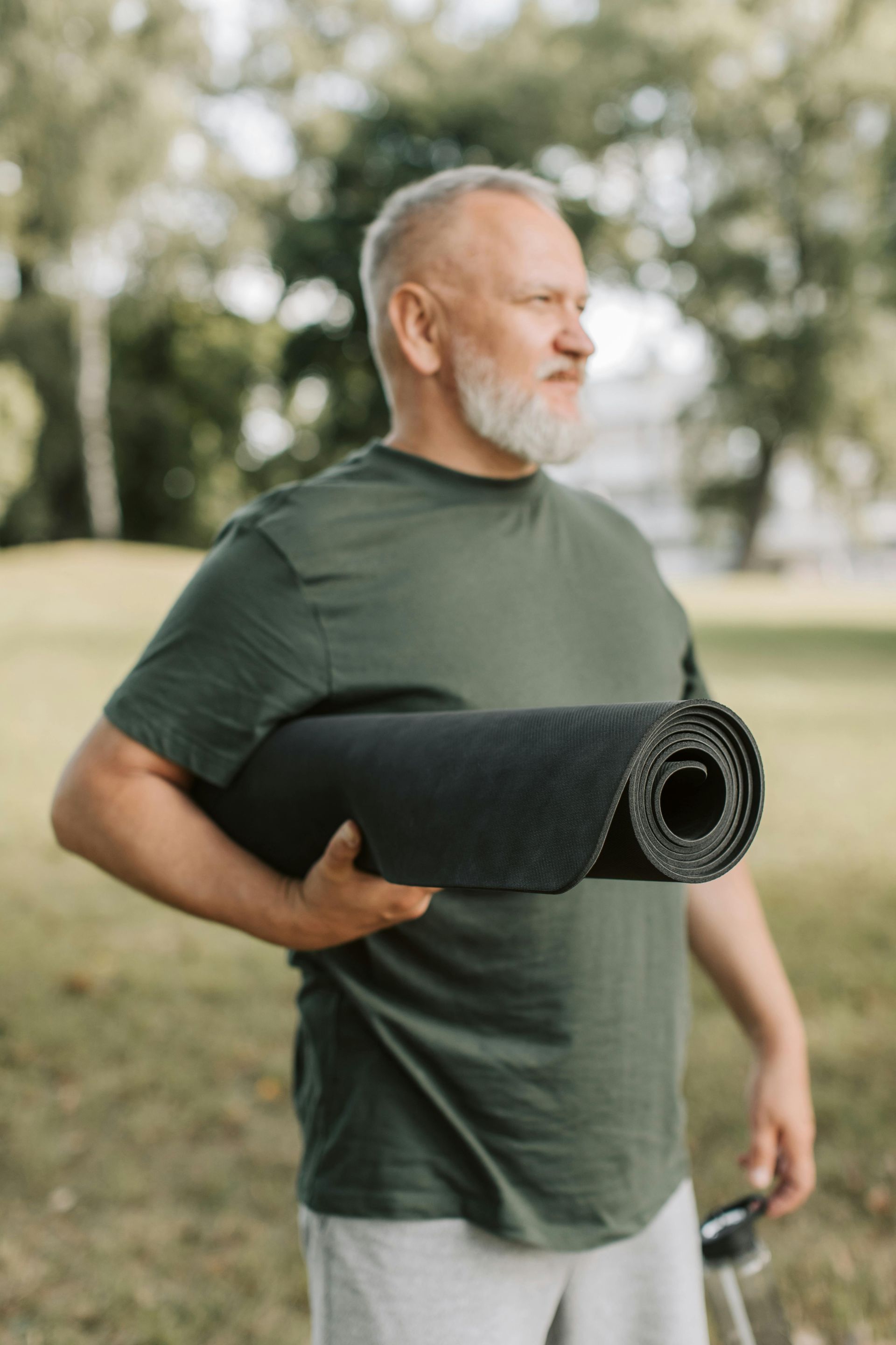 Woman in pink leggings and grey jacket holding yoga mat in park.