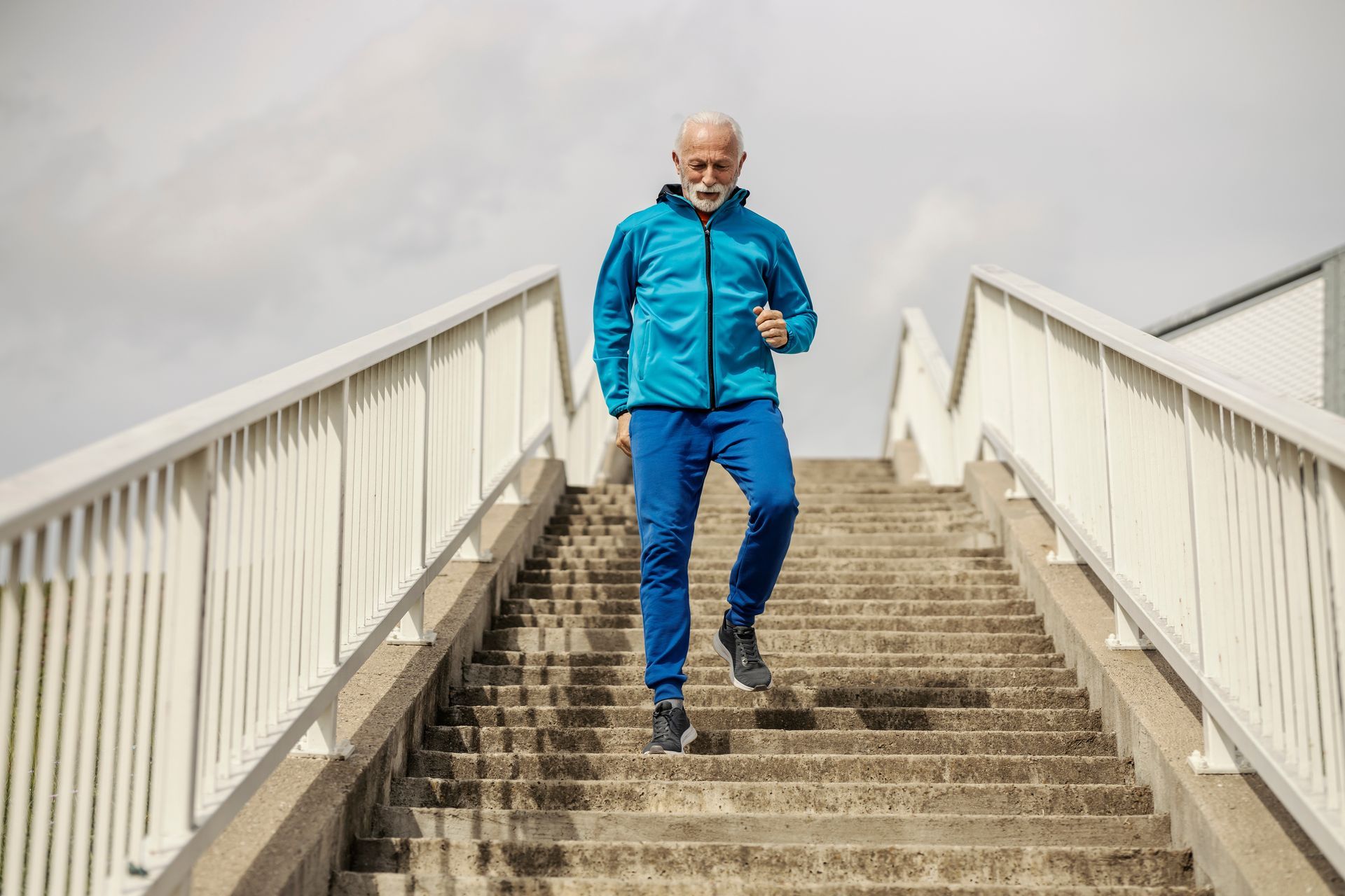 Man in blue workout clothes descends outdoor concrete stairs.