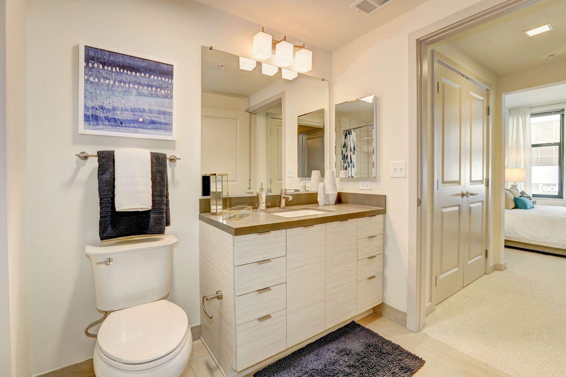 Bright bathroom with double vanity, toilet, mirror, and doorway to a bedroom at Solaire 7077 Woodmont in Bethesda, MD.