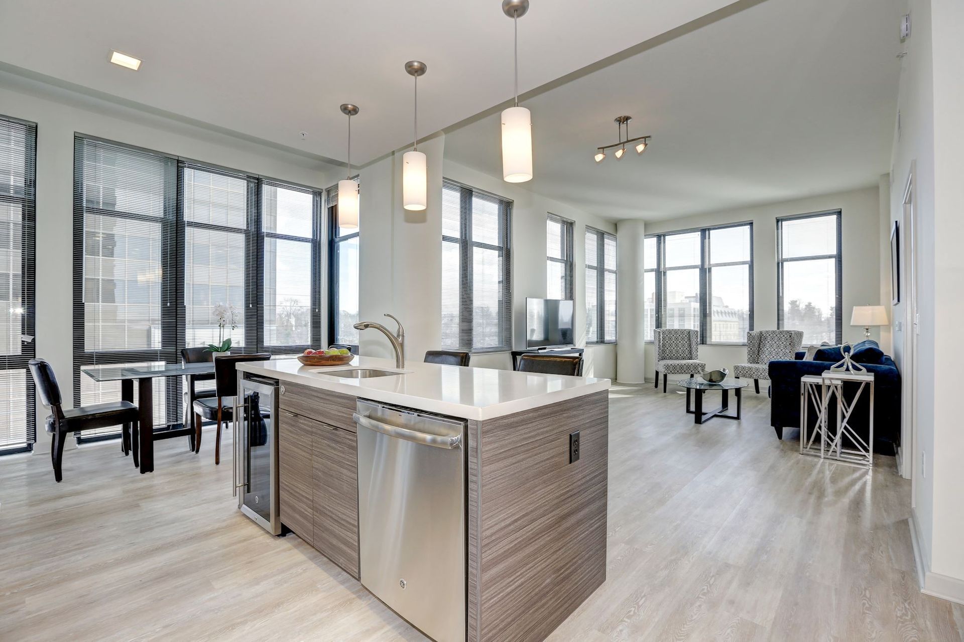 Modern open kitchen and dining area with island, bar stools, large windows, and light wood floors at Solaire 7077 Woodmont in Bethesda, MD.