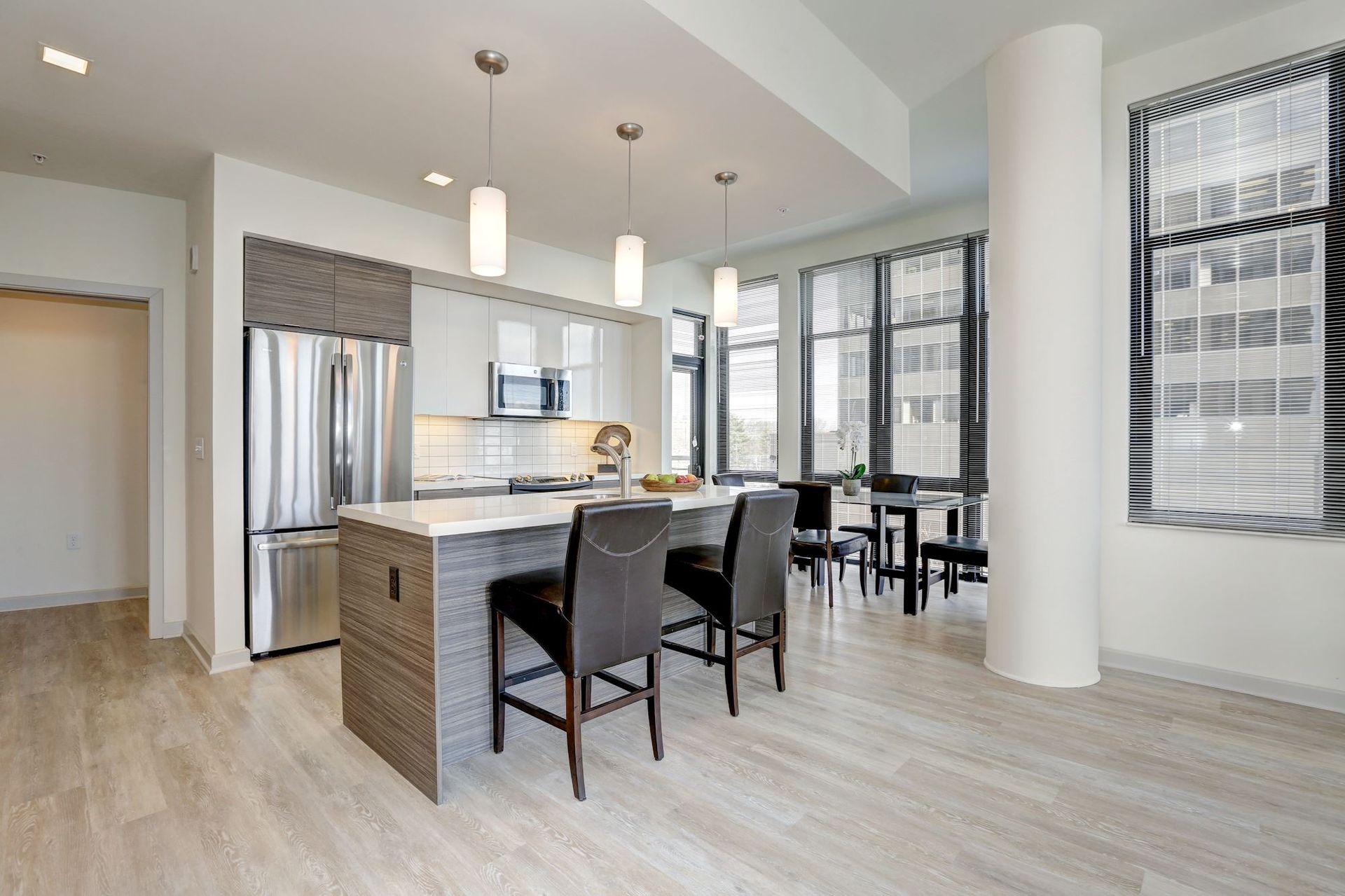 Bright modern kitchen with island, black stools, stainless steel appliances, and large windows at Solaire 7077 Woodmont in Bethesda, MD.