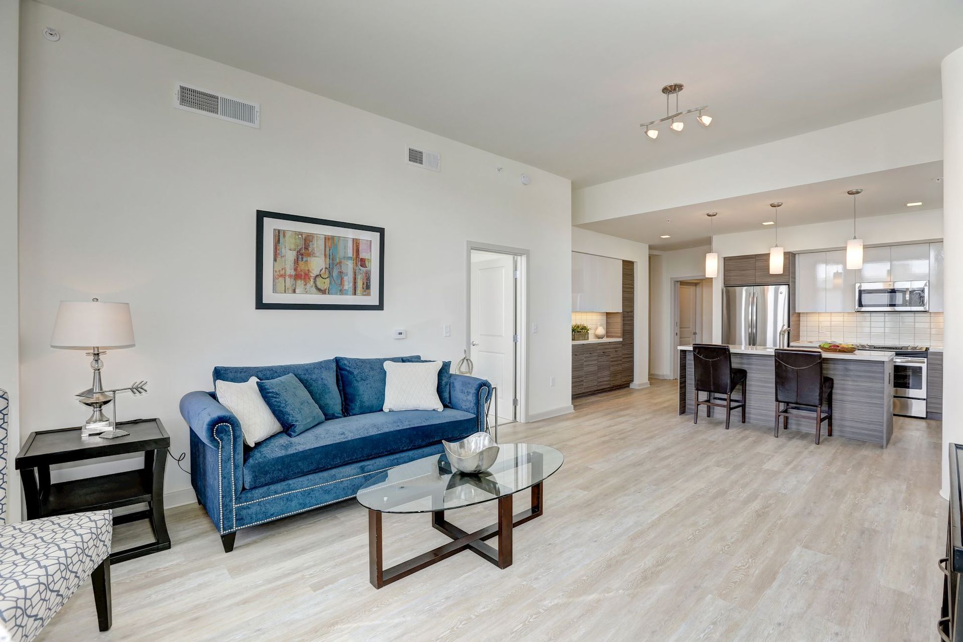 Bright living room with blue sofa, glass coffee table, and open kitchen in the background at Solaire 7077 Woodmont in Bethesda, MD.