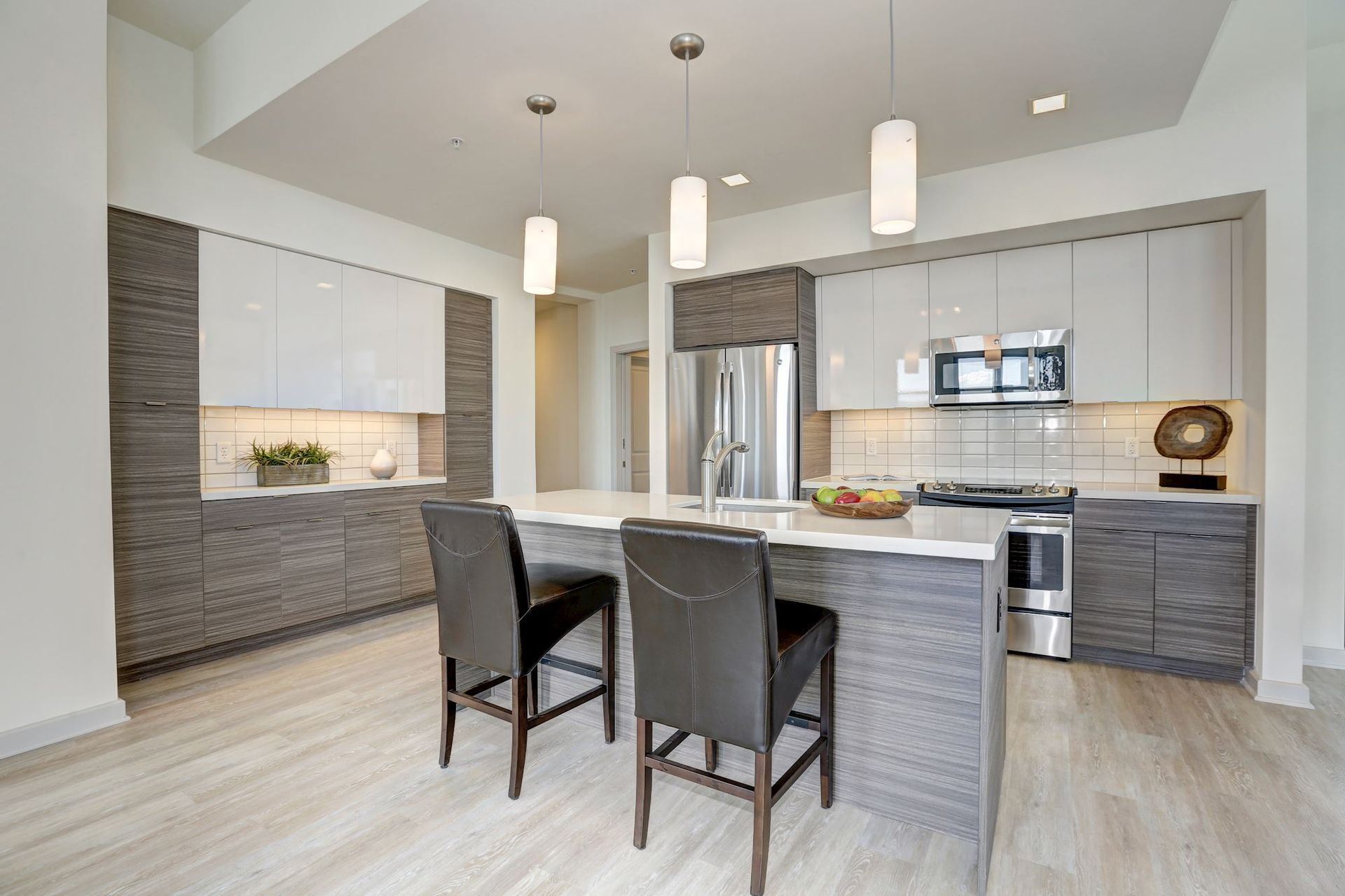 Modern kitchen with gray cabinets, island, pendant lights, and two chairs in a bright open layout at Solaire 7077 Woodmont in Bethesda, MD.
