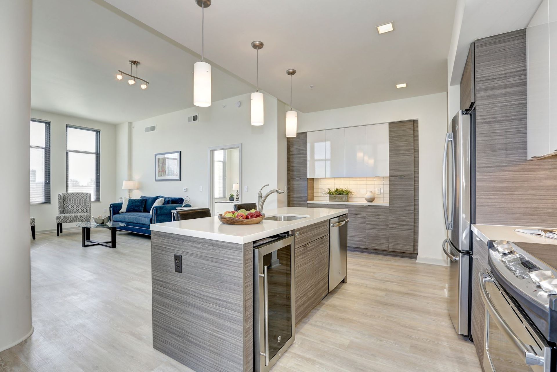 Bright modern kitchen and living room with island, gray cabinets, blue sofa, and high ceilings at Solaire 7077 Woodmont in Bethesda, MD.