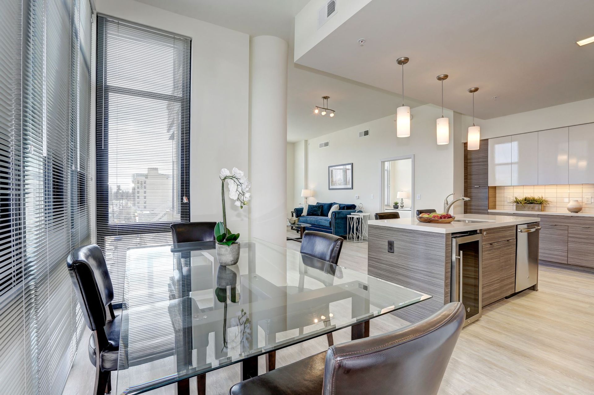 Bright modern dining and kitchen area with glass table, black chairs, and island stools at Solaire 7077 Woodmont in Bethesda, MD.