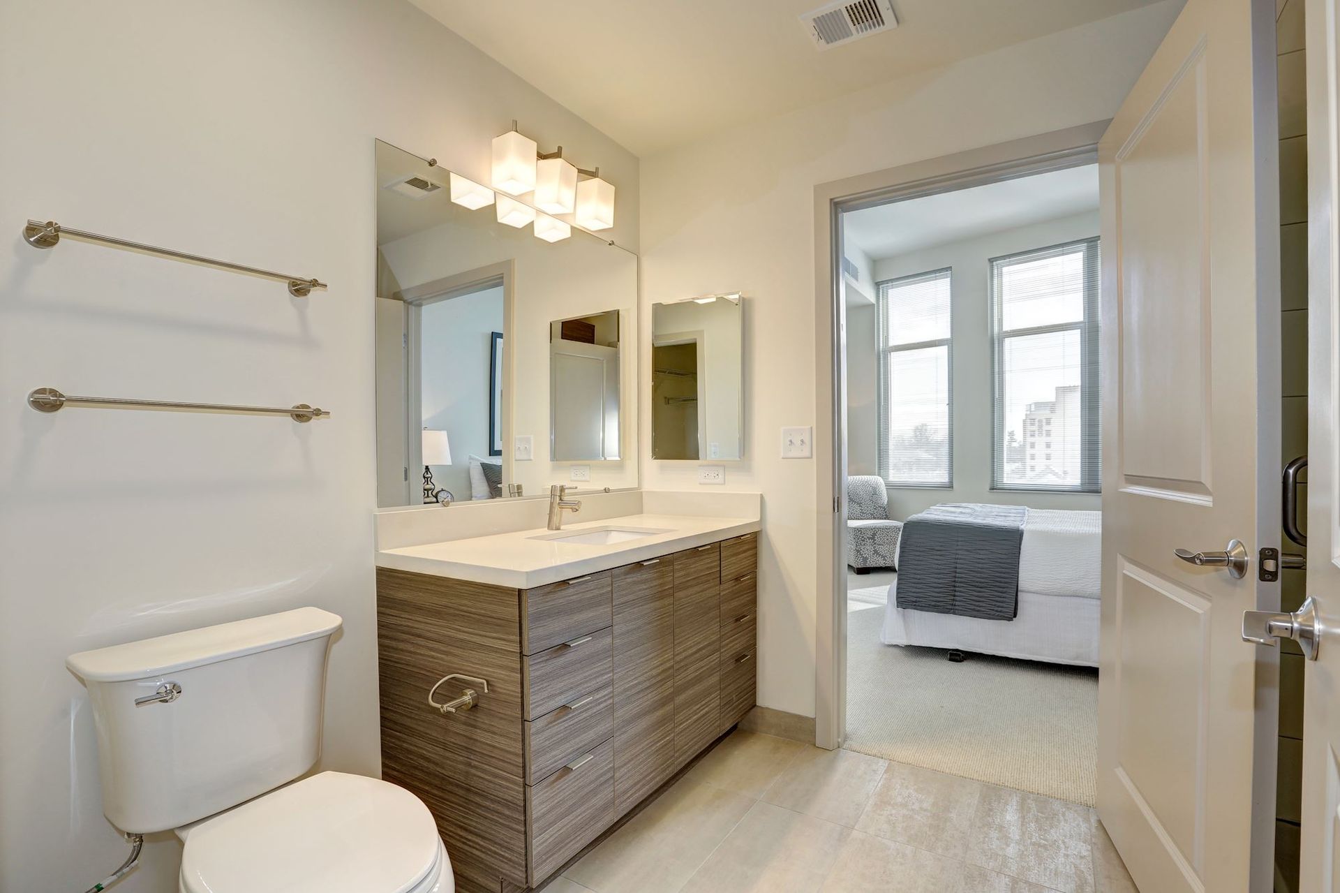 Bright bathroom with double vanity, toilet, and an open door to a bedroom at Solaire 7077 Woodmont in Bethesda, MD.