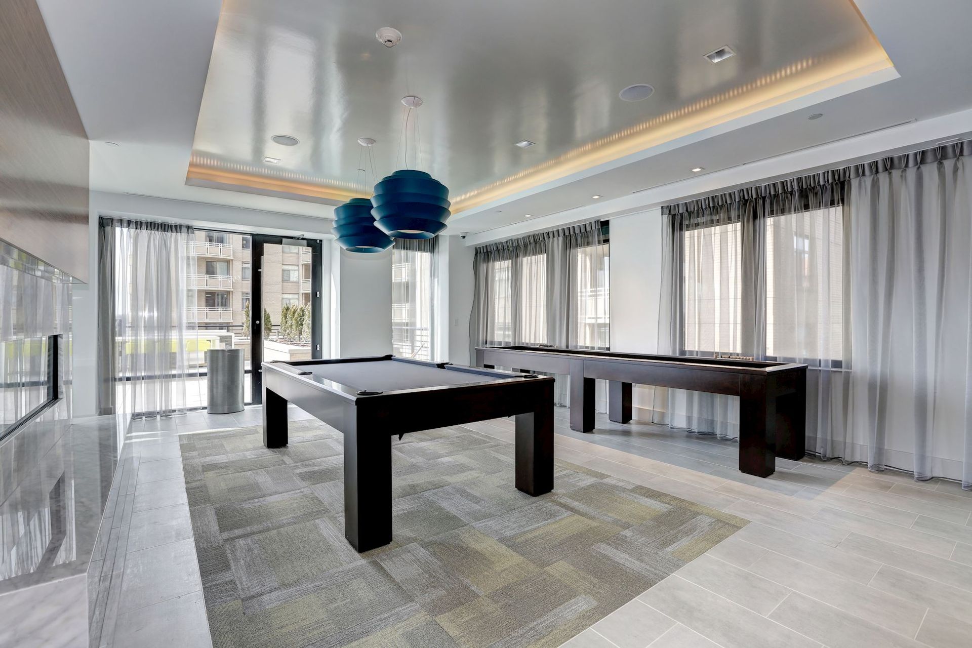 Modern dining room with a black table, blue pendant light, and floor-to-ceiling curtains at Solaire 7077 Woodmont in Bethesda, MD.
