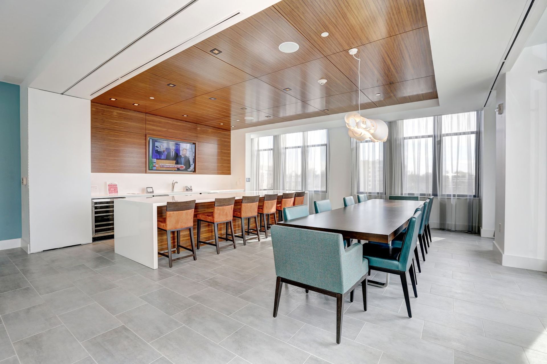 Modern conference room with a long table, orange stools, a wall-mounted TV, and large windows at Solaire, 7077 Woodmont, in Bethesda, MD.