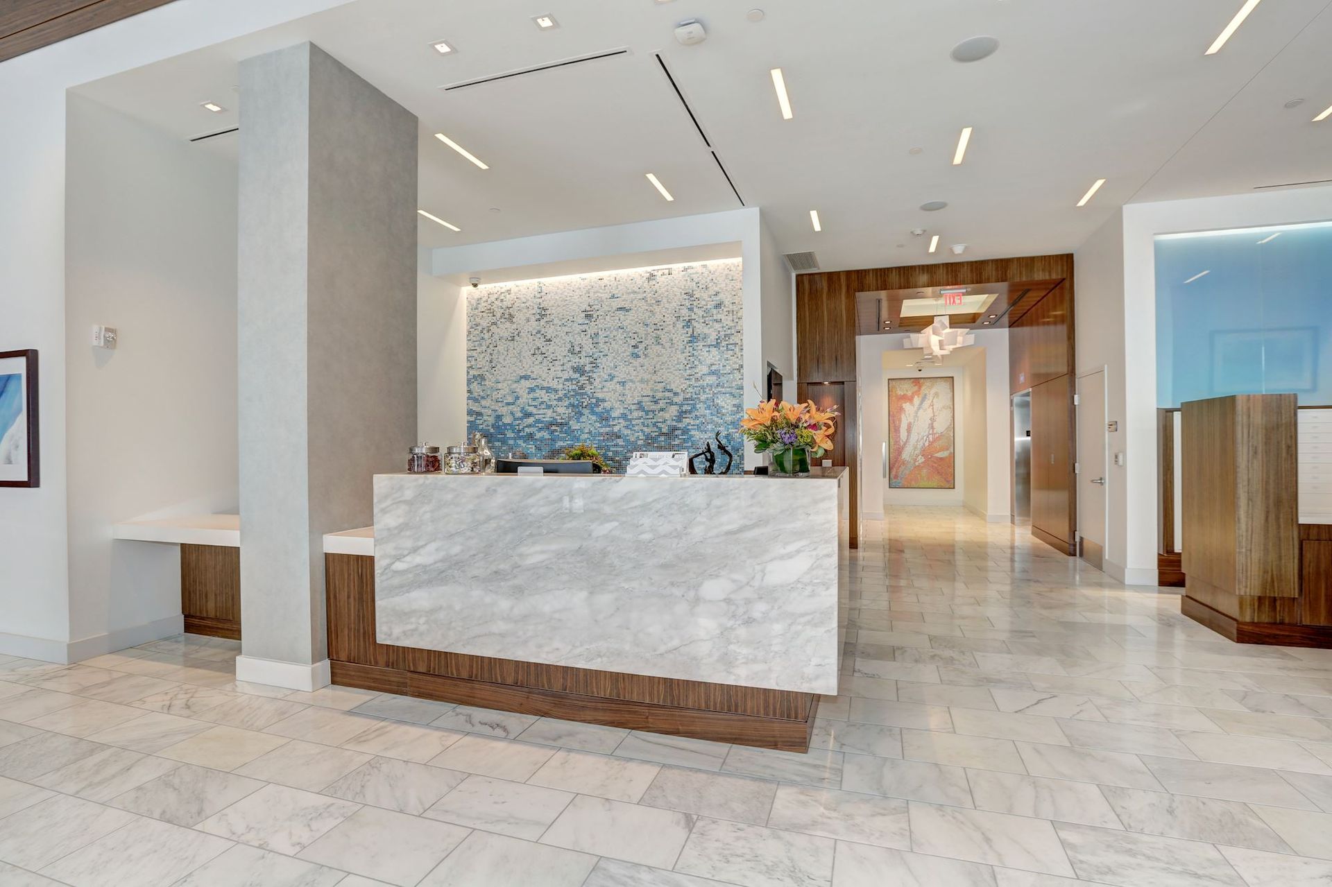 Bright hotel lobby with marble floors, white reception desk, floral wall art, and wooden accent panels at Solaire 7077 Woodmont in Bethesda, MD.