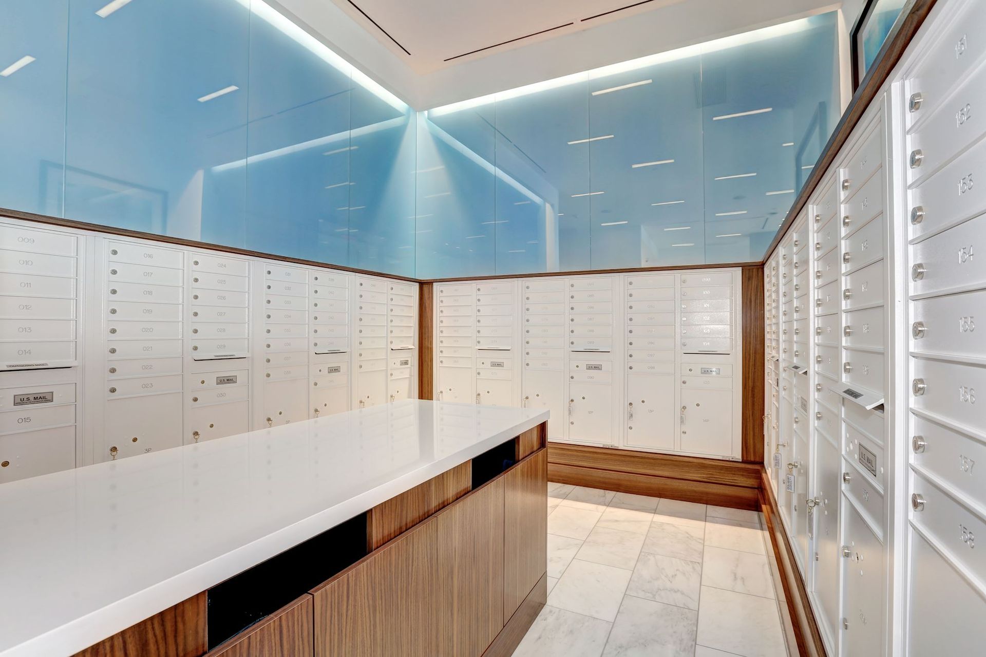 Modern mailroom with white lockers, wood accents, and a long counter in a bright, clean space at Solaire 7077 Woodmont in Bethesda, MD.