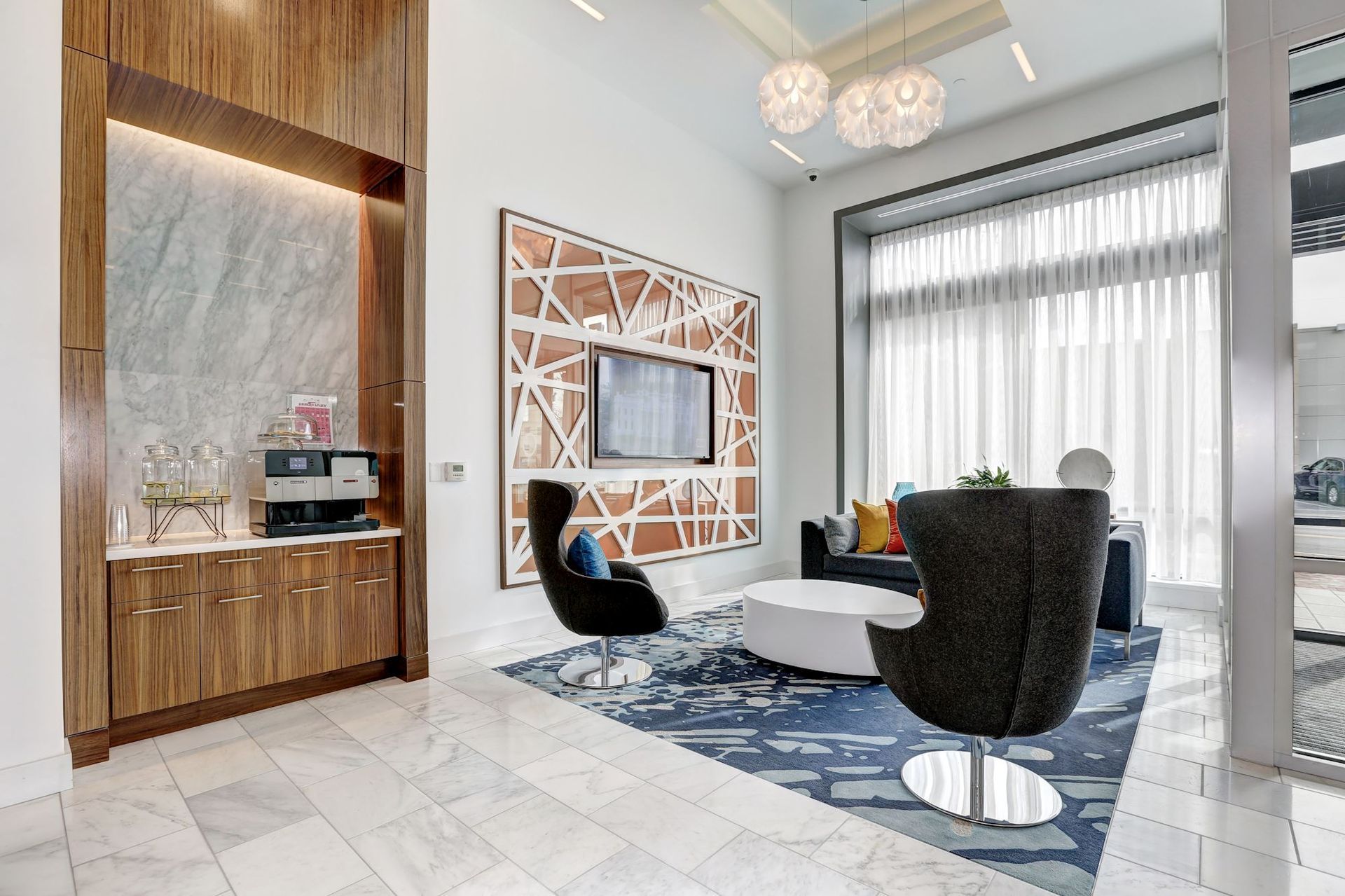 Modern lounge with white chairs, blue rug, wood accent wall, and large windows at Solaire 7077 Woodmont in Bethesda, MD.