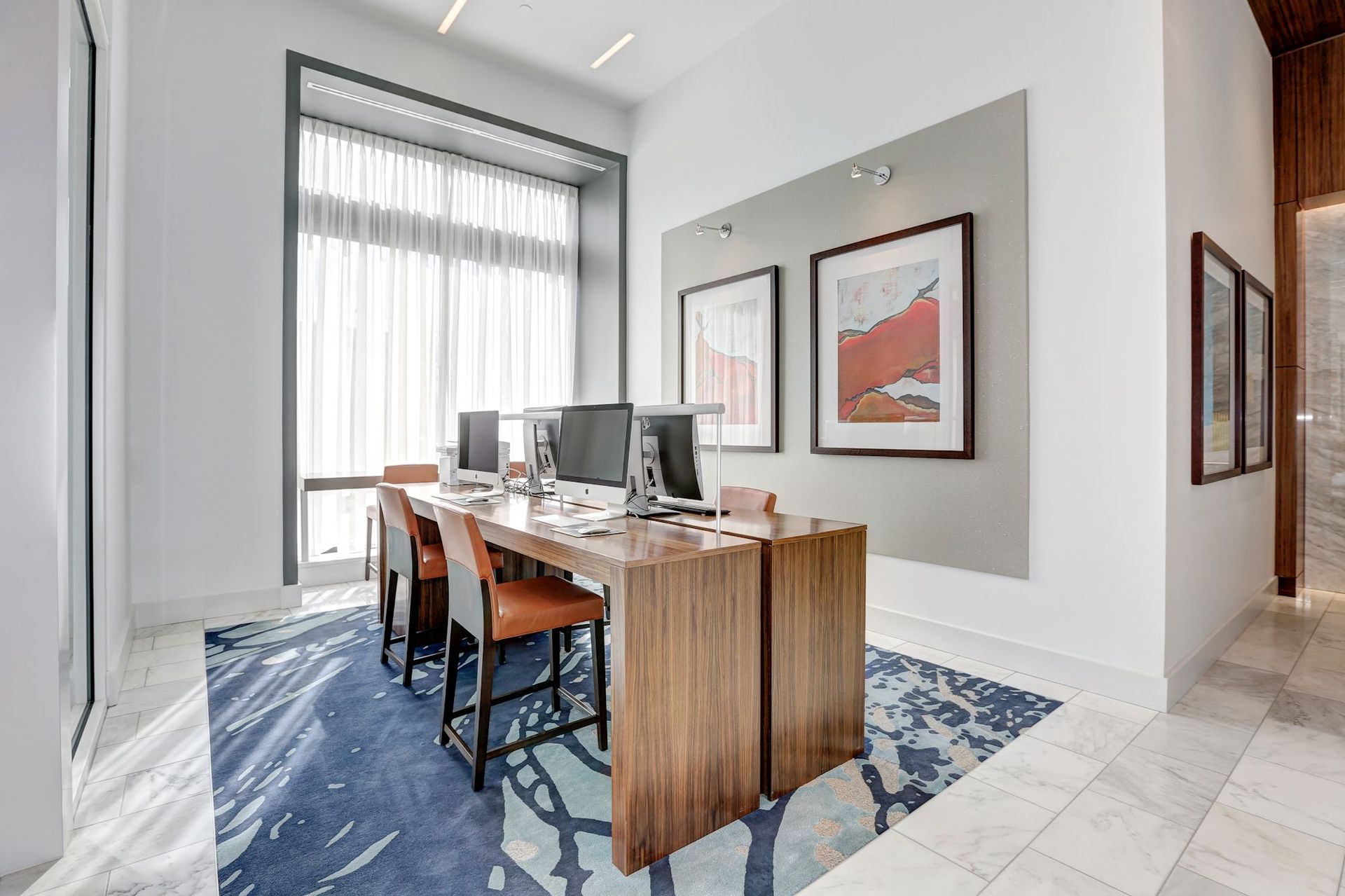 A room with a desk, chairs, computers, and paintings on the wall at Solaire 7077 Woodmont in Bethesda, MD.
