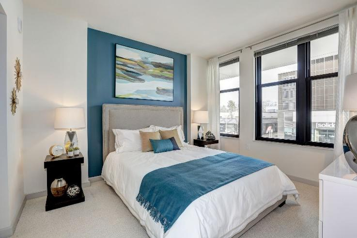 Bright bedroom with blue accent wall, white bedding, and large windows at Solaire 7077 Woodmont in Bethesda, MD.