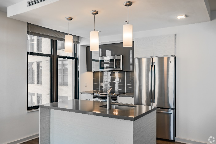 Modern kitchen with stainless steel appliances, white cabinets, dark island, and pendant lights at Solaire 7077 Woodmont in Bethesda, MD.