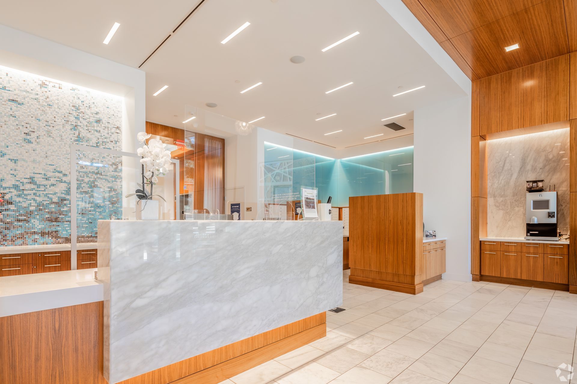 Modern hotel lobby with white marble reception desk, wood accents, and bright recessed lighting at Solaire 7077 Woodmont in Bethesda, MD.