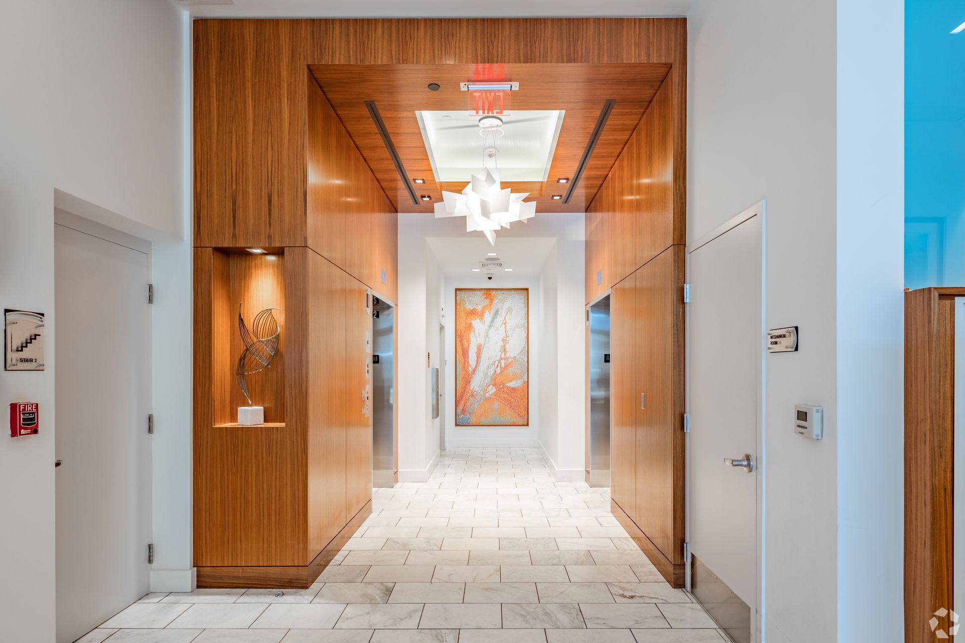 Modern hotel hallway with wood-paneled walls, white tile floor, and framed art at the far end at Solaire 7077 Woodmont in Bethesda, MD.
