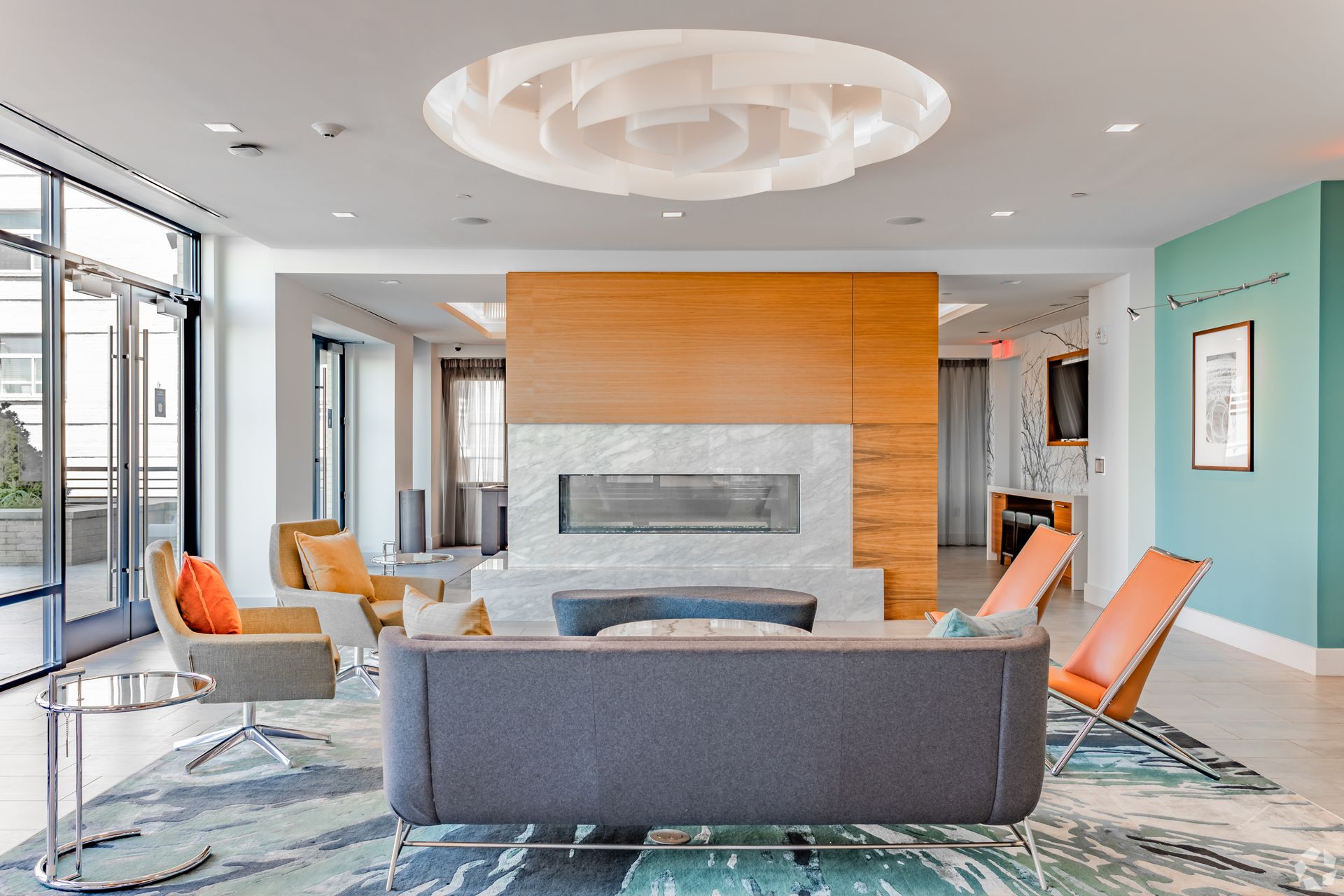 Modern lobby lounge with gray seating, orange chairs, a fireplace, and large windows at Solaire 7077 Woodmont in Bethesda, MD.