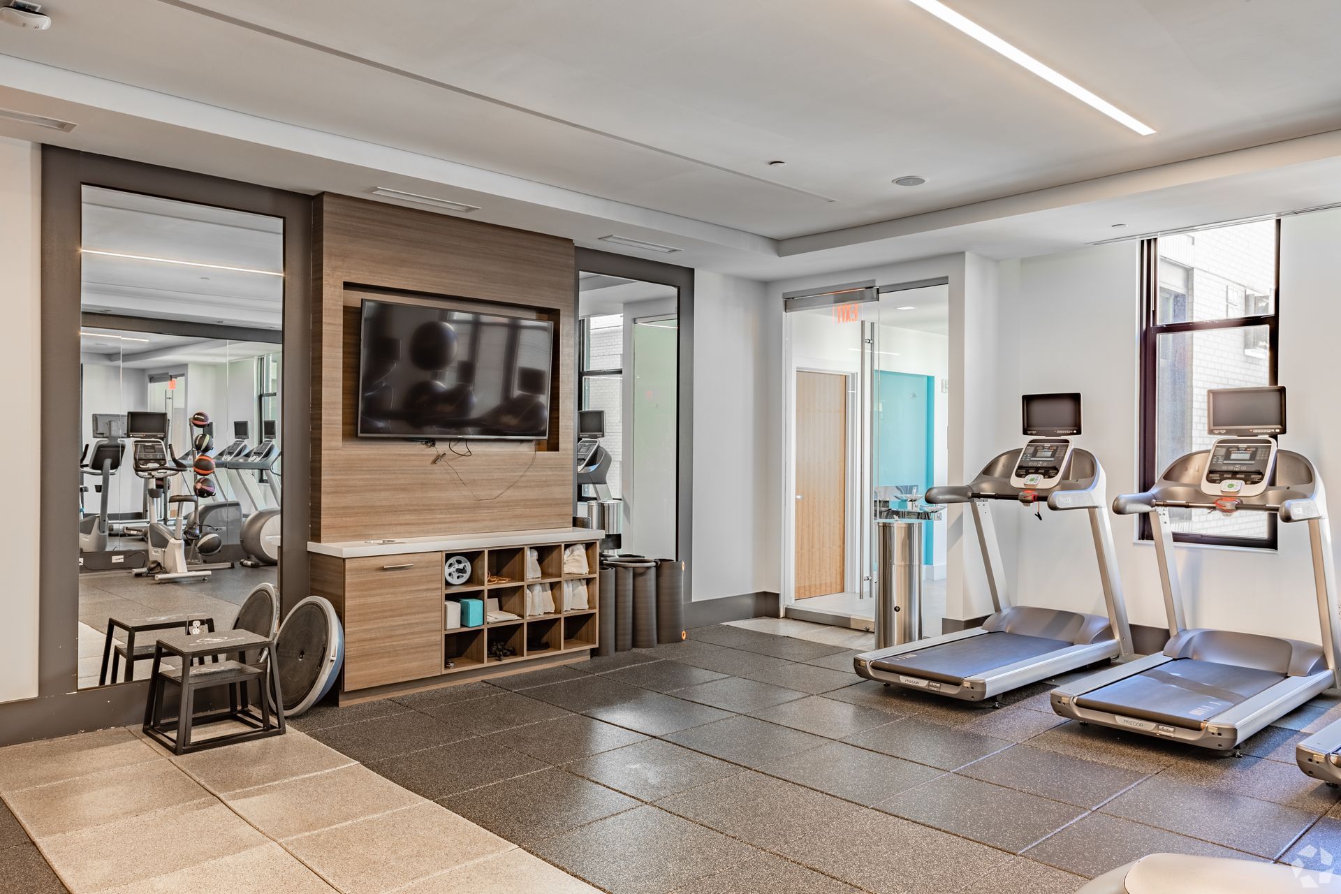 Modern gym interior with treadmills, weight machines, mirrors, and a wall-mounted TV at Solaire 7077 Woodmont in Bethesda, MD.