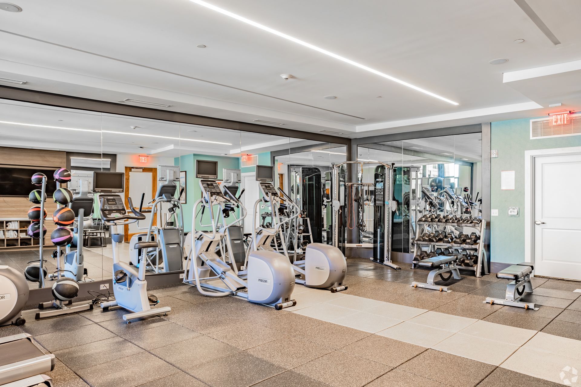 Modern gym with exercise machines, mirrors, and bright overhead lighting at Solaire 7077 Woodmont in Bethesda, MD.