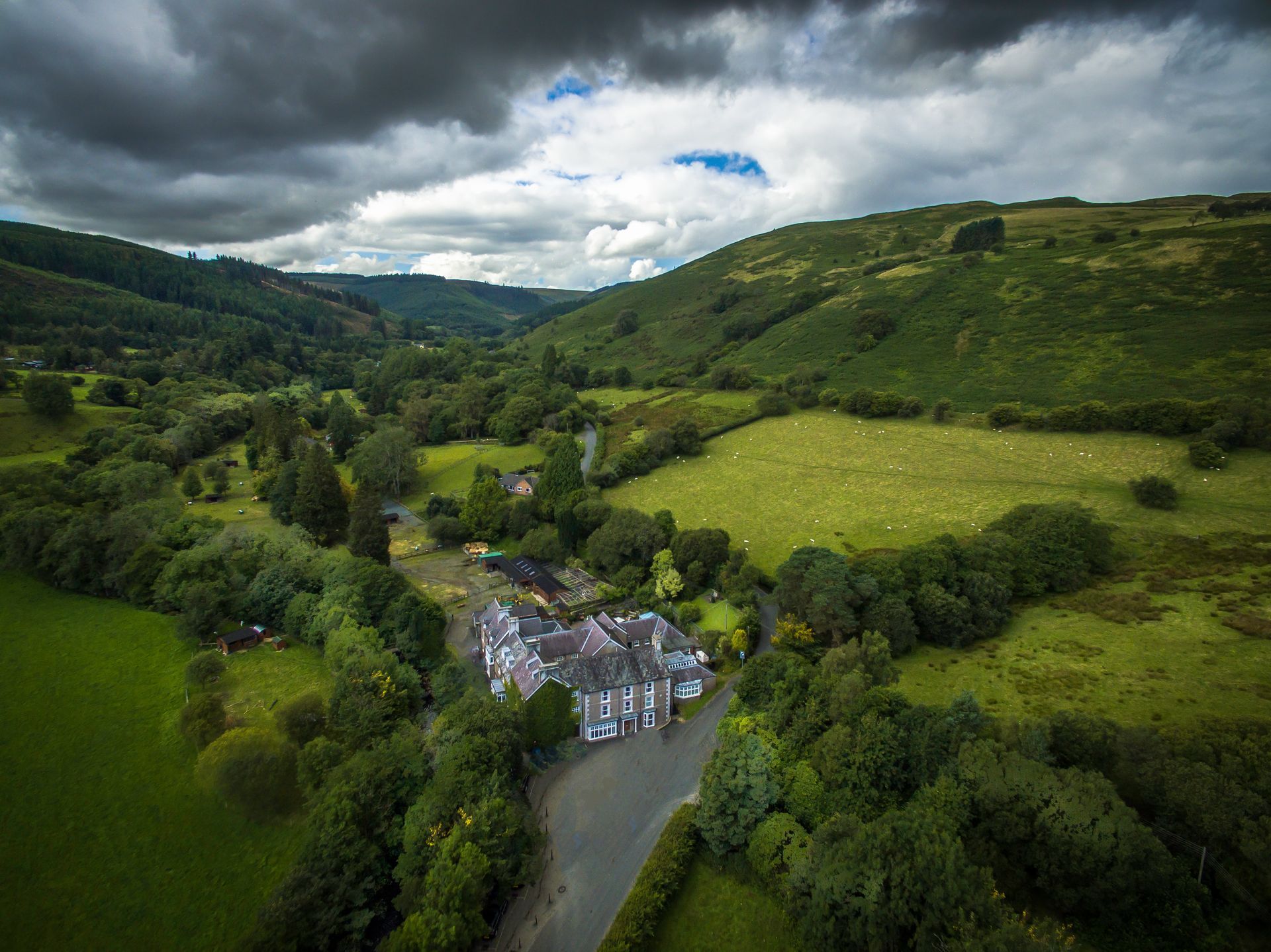 Aerial view of a white building beside a river in a lush green valley under cloudy skies
