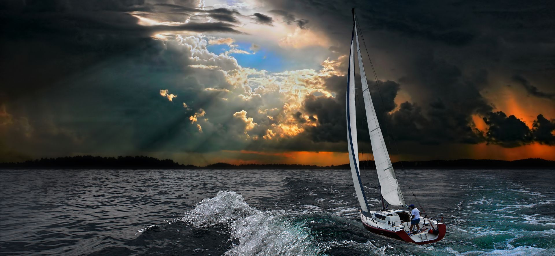 Sailboat cutting through dark waves under a dramatic sunset sky with glowing clouds