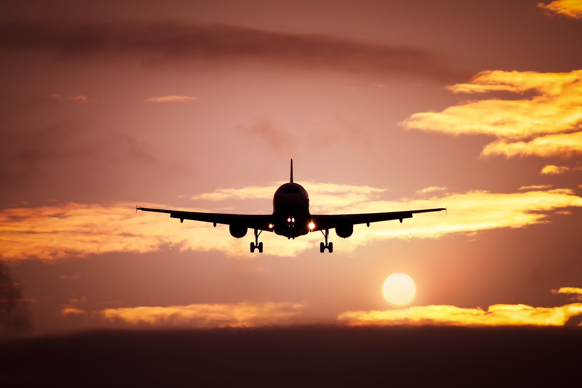 Silhouetted airplane approaching runway at sunset with orange clouds and glowing sun