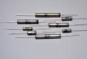 Assorted metal cylindrical fuses with wire leads arranged on a light gray background