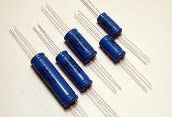 Four blue cylindrical electronic components with metal leads on a white background