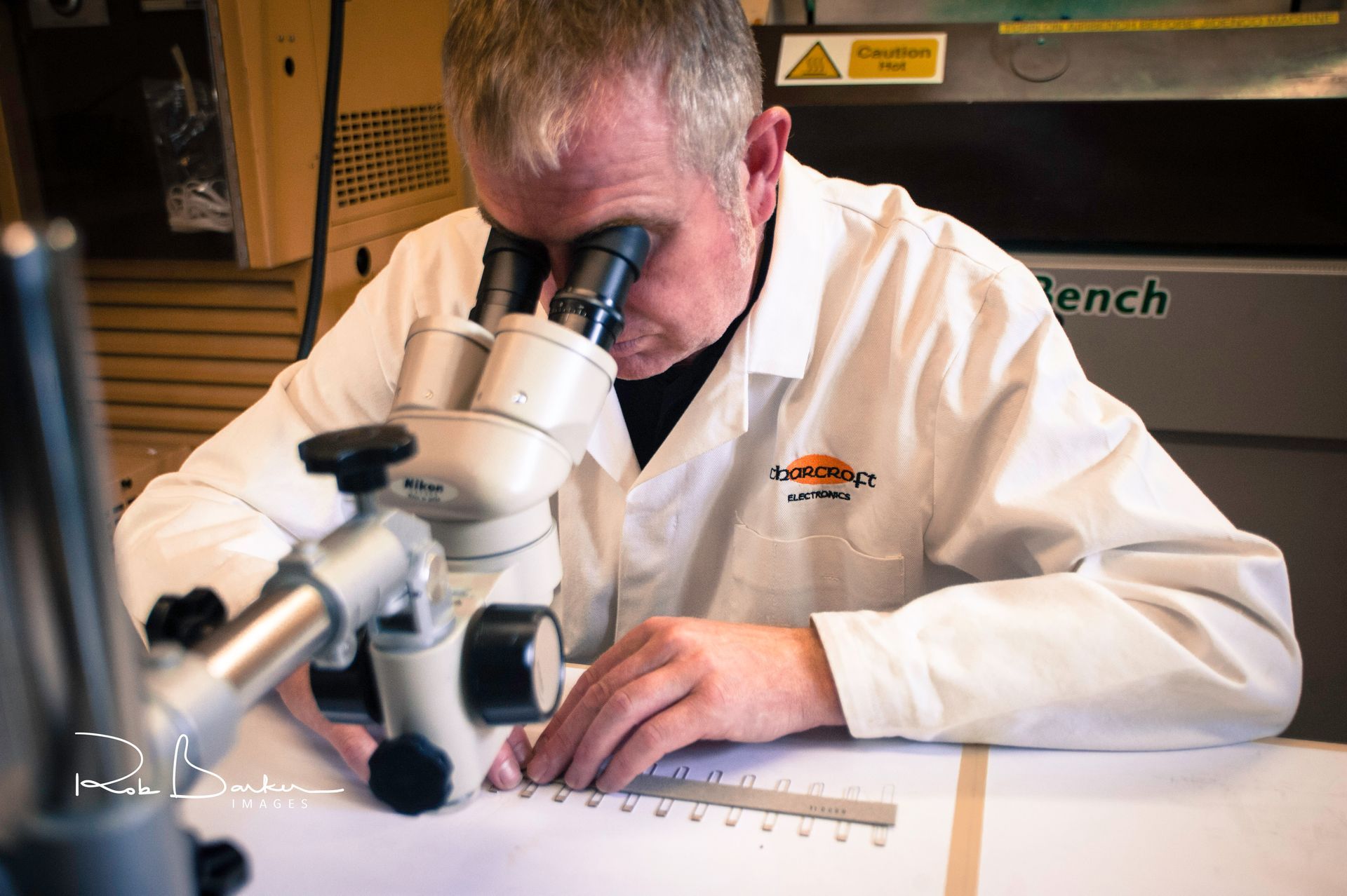 Scientist in white lab coat examining a specimen with a microscope at a lab bench