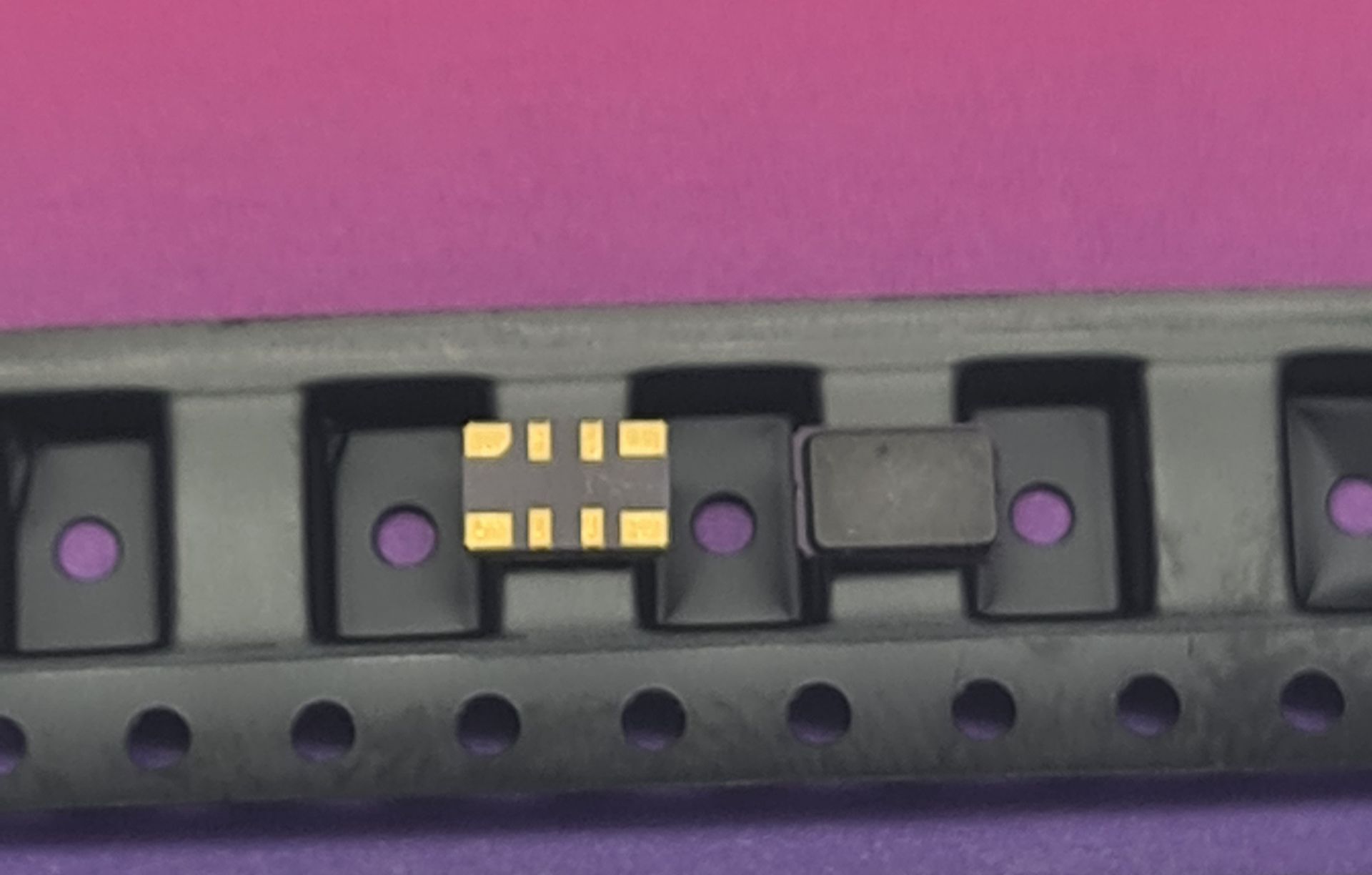 Close-up of a black device with purple buttons and a small gold connector on a pink background