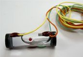 Small homemade electronic device with wires and a red LED on a white background