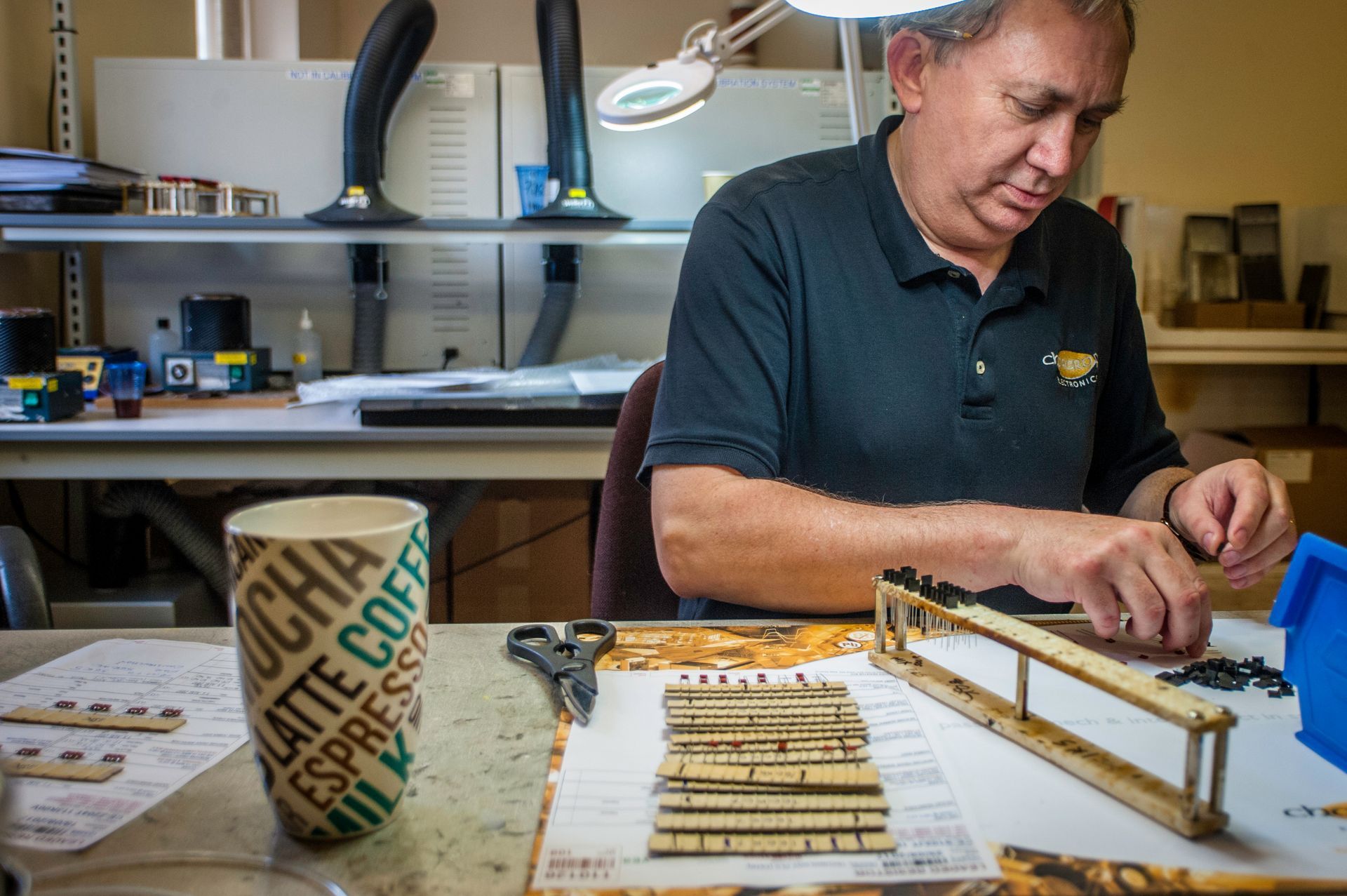 Man in a workshop carefully assembling a wooden model beside a paper cup and tools