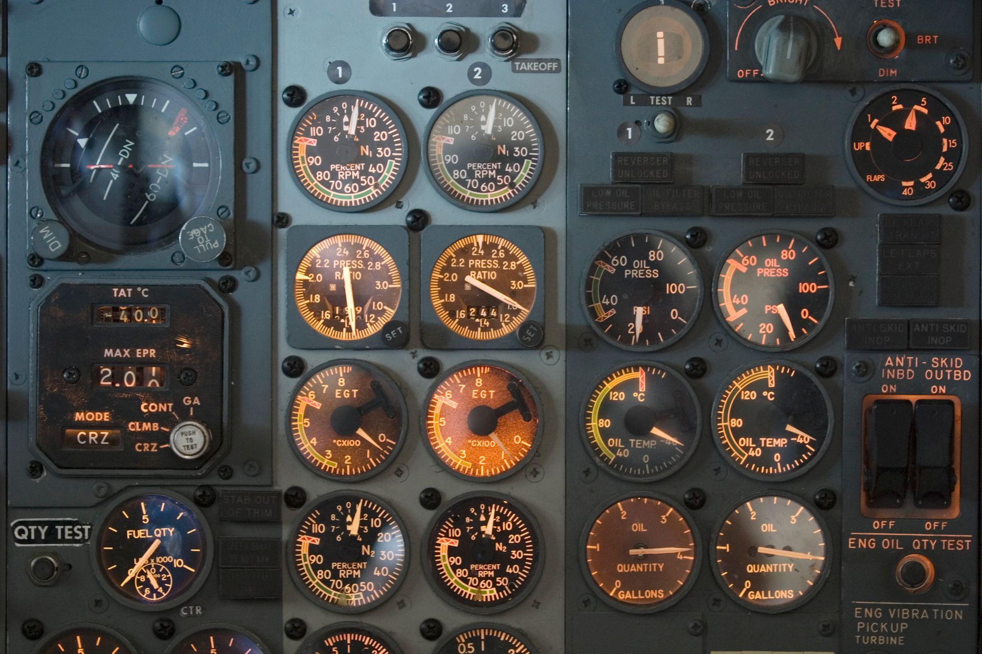 Aircraft cockpit panel filled with illuminated analog gauges and dials in dark gray and amber