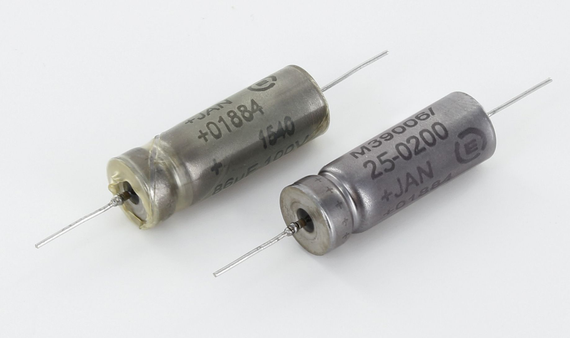 Two small cylindrical metal electronic components with wire leads on a white background
