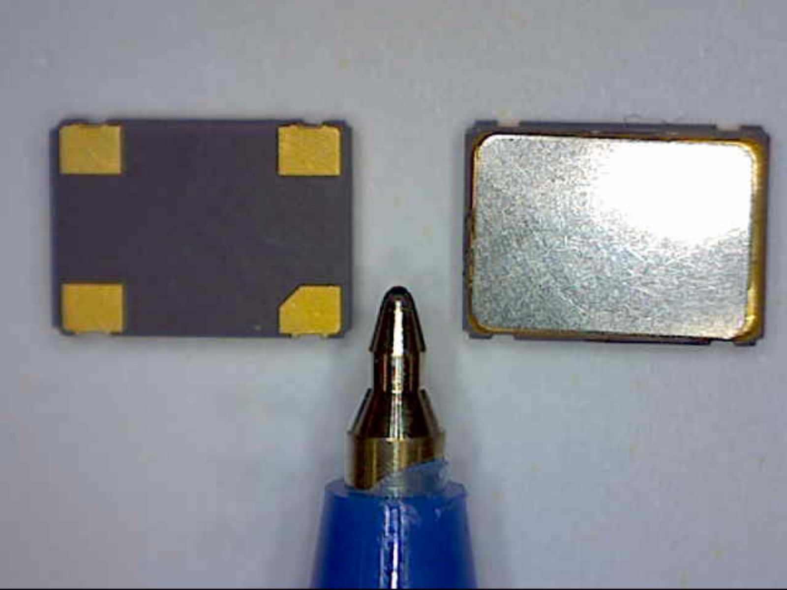 Electronic component between a pen tip and a small metal plate on a gray surface
