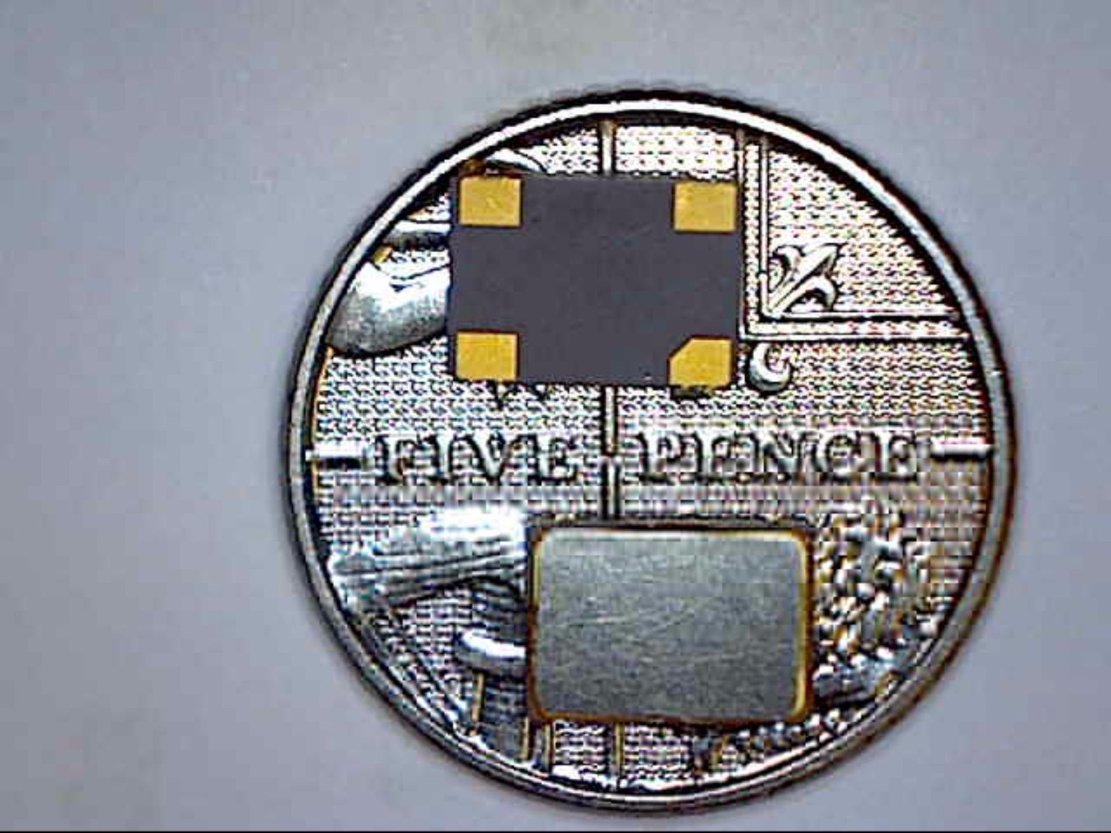 Coin with a small circuit board chip and a metal contact pad attached to it.