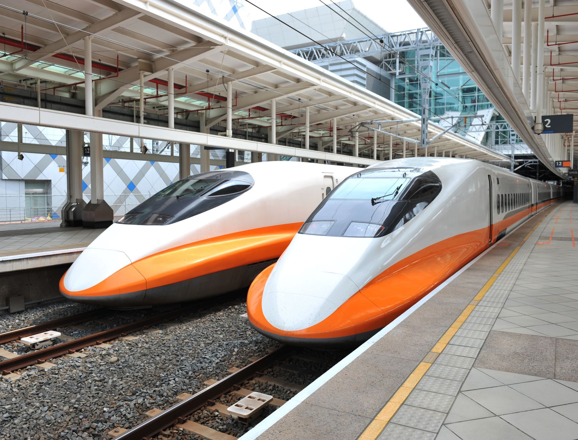 Two white-and-orange high-speed trains stopped at a modern train platform.
