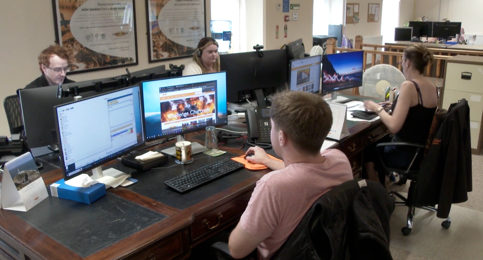 People working at computers in an office with multiple desks and monitors