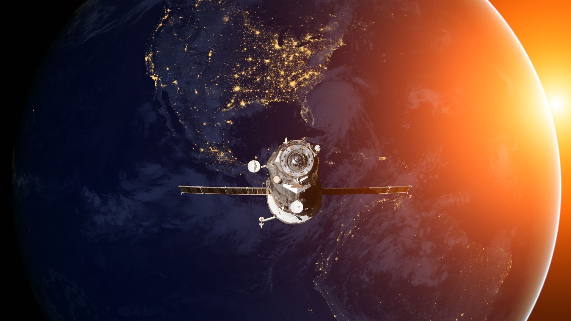 Spacecraft with solar panels silhouetted against Earth, with bright city lights and sunrise at the planet’s edge