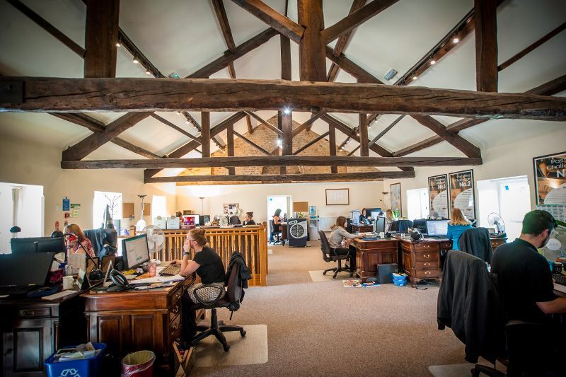 Open office with exposed wooden beams and people working at desks in a bright loft space