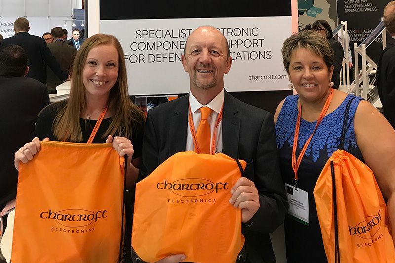 Three people at a trade show holding orange CharacTour bags and smiling at the camera