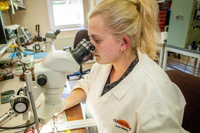 Scientist using a microscope in a laboratory, wearing a white lab coat, with lab equipment in the background