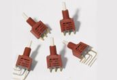 Five red wire connector plugs with metal prongs on a white background