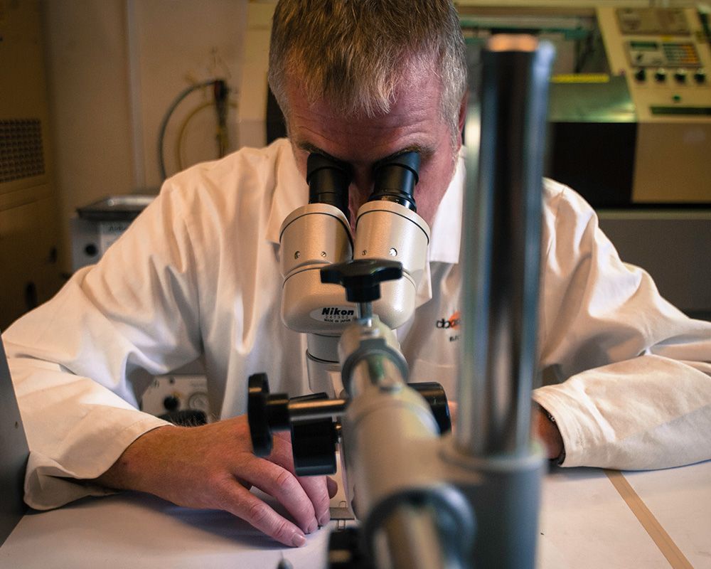 Scientist in a lab coat looking through a microscope at a laboratory bench