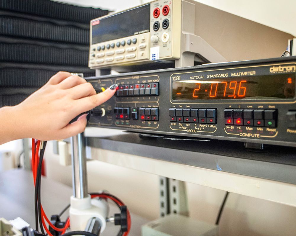Hand adjusting controls on an electronic lab instrument with orange digital display in a workshop setup