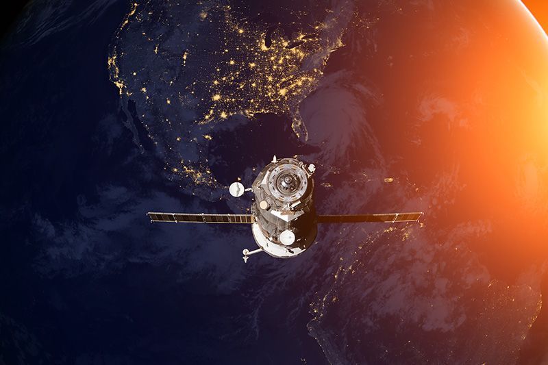 Satellite orbiting Earth with city lights glowing below and a bright orange sunrise at the edge of space